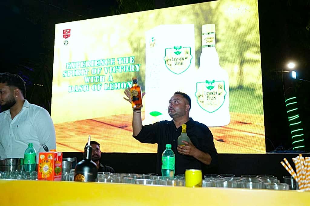 Bartender pouring under a bright LED brand wall at an outdoor evening programme