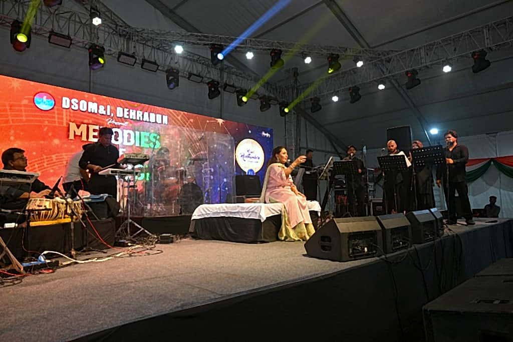 Female vocalist performing seated on stage with live musicians and LED backdrop