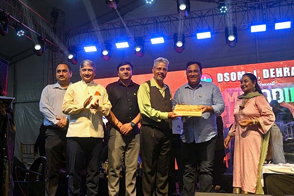 Award presentation on stage with guests holding a wooden plaque under LED branding