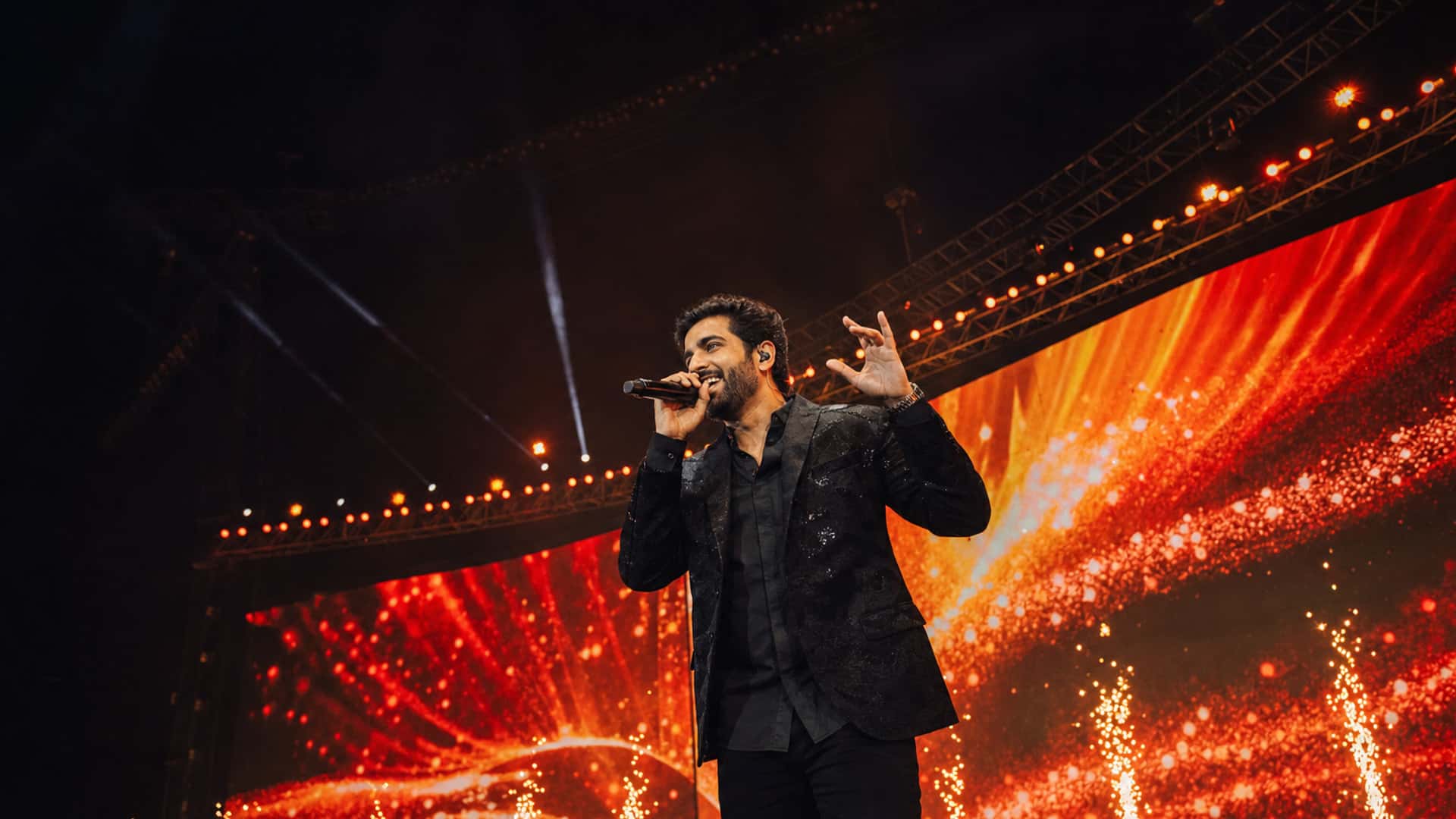 Solo live performer on a cinematic LED stage with warm spotlights and cold spark fountains, no audience in frame